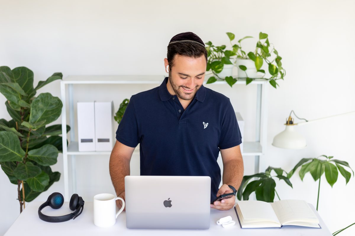 Abe Braha reading a message on his phone at a laptop
