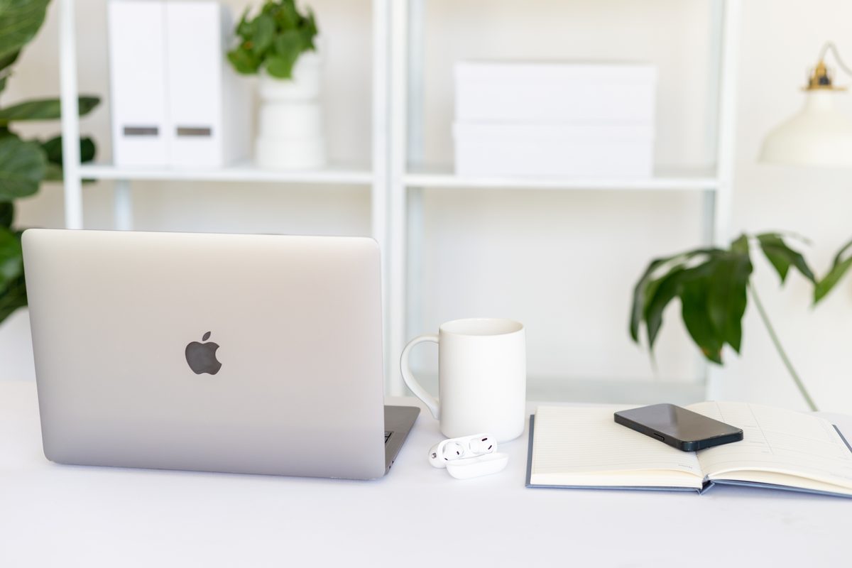 An empty desk with a laptop, a mug, earbuds and an open notebook
